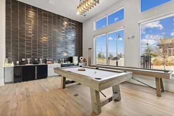 A pool table is in the middle of a room with a kitchen in the background.